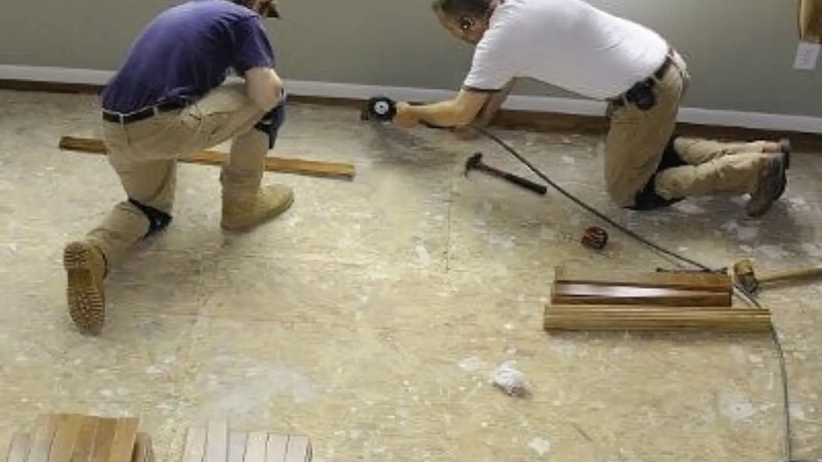 Two workers kneeling on a subfloor installing new flooring